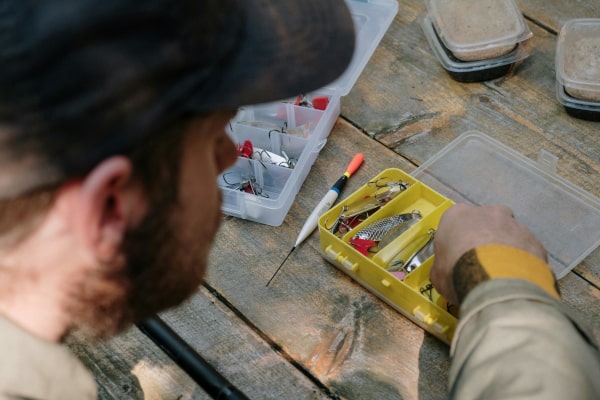 Pêcheur choisissant ses leurres dans sa boîte de matériel de pêche sur une table en bois